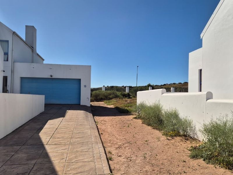 Front exterior view of the property featuring a paved driveway, a blue garage door, and white boundary walls under a clear sky.