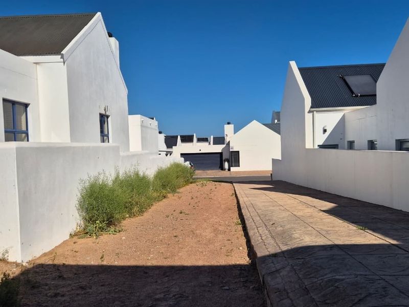 View of the property entrance featuring a paved driveway, white exterior walls, and modern gabled roof architecture within a residential estate.