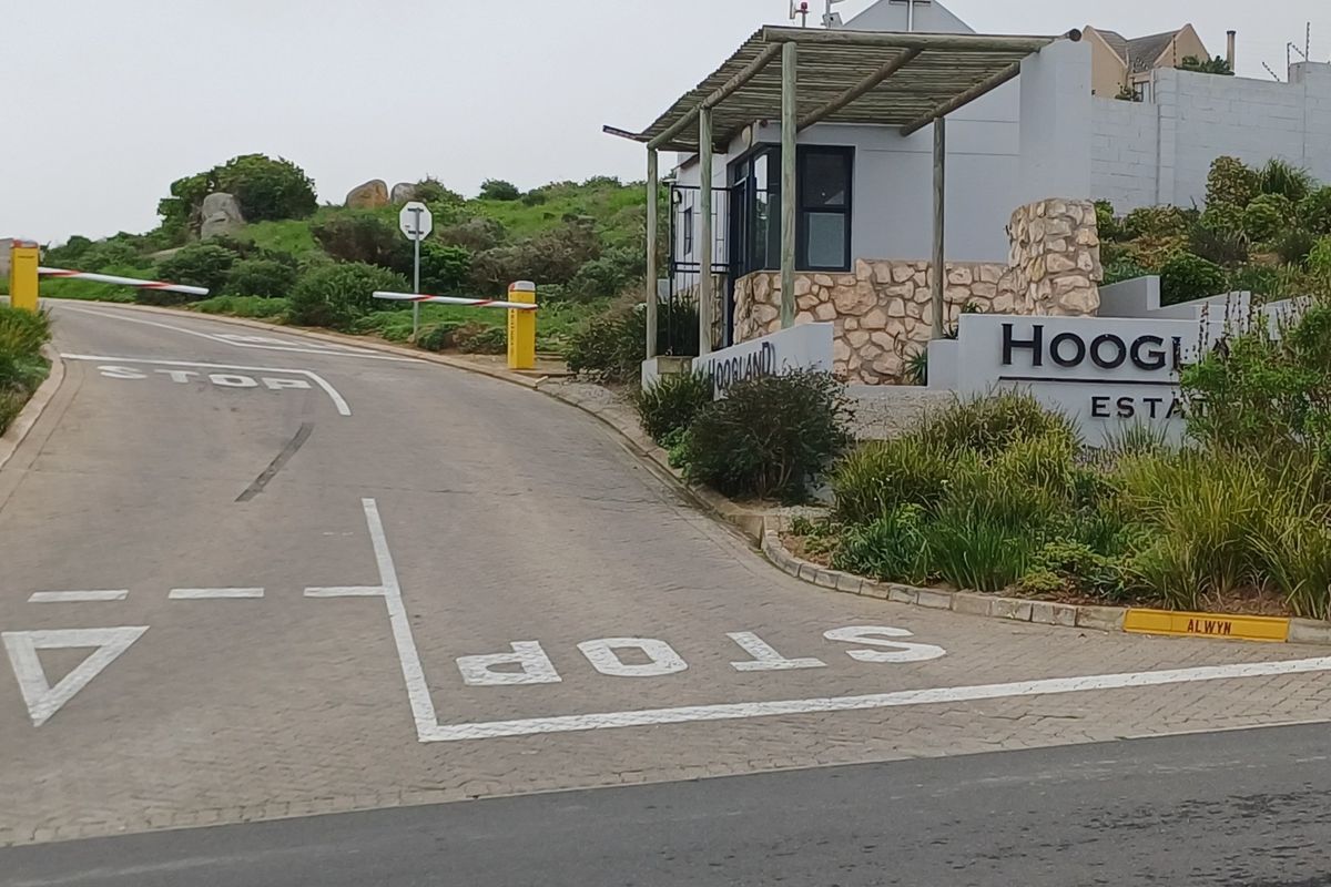 The entrance to Hoogland Estate featuring a paved driveway, security boom gate, and a stone-clad guard house.
