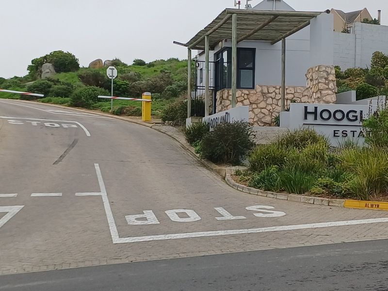 The entrance to Hoogland Estate featuring a paved driveway, security boom gate, and a stone-clad guard house.