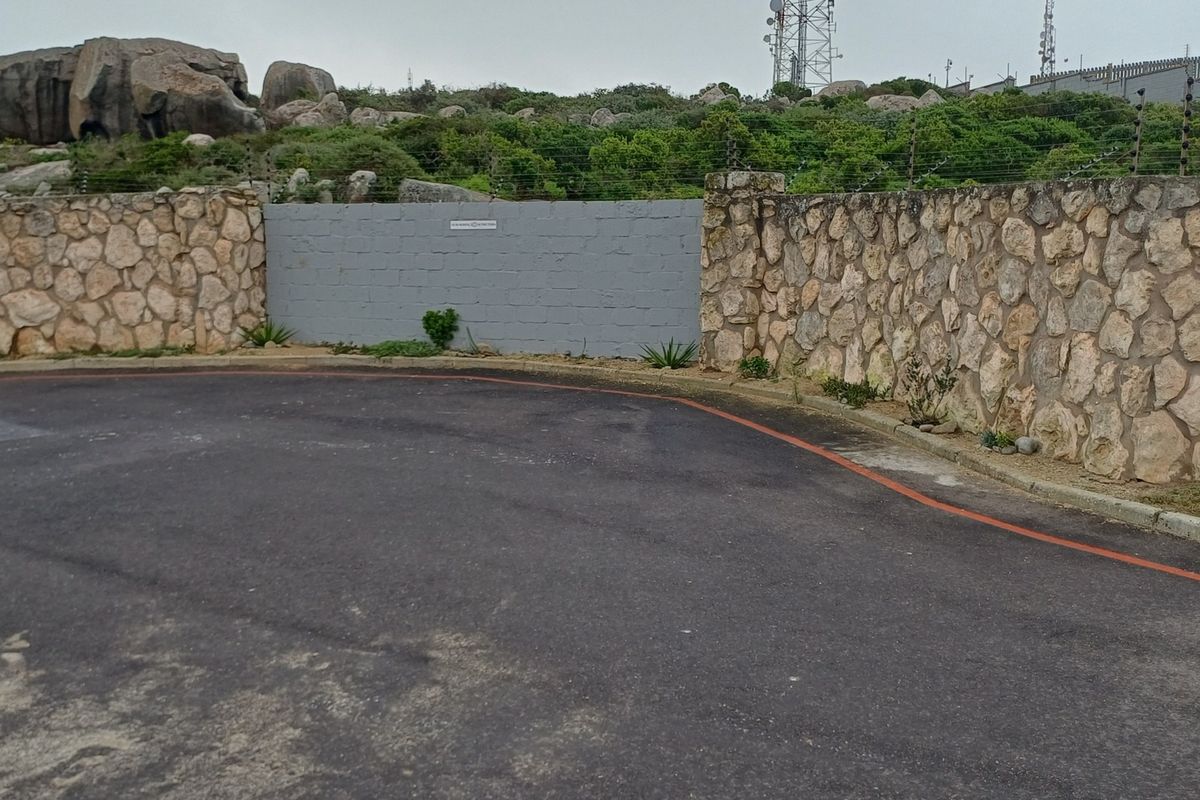 A view of the property boundary featuring a stone and concrete block wall with integrated electric fencing and an asphalt driveway entrance.