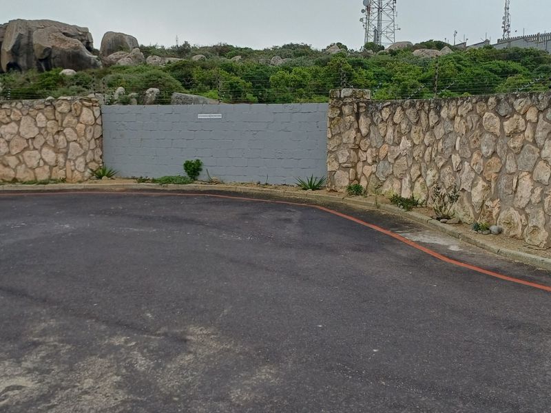 A view of the property boundary featuring a stone and concrete block wall with integrated electric fencing and an asphalt driveway entrance.