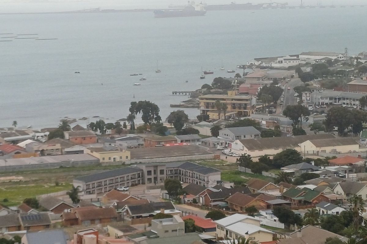 An elevated aerial view overlooking a coastal town, harbour, and surrounding residential area.