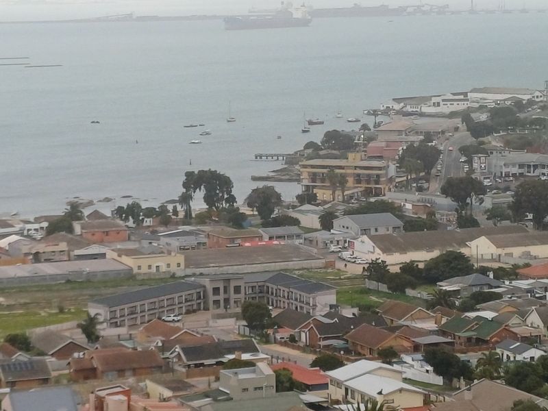 An elevated aerial view overlooking a coastal town, harbour, and surrounding residential area.