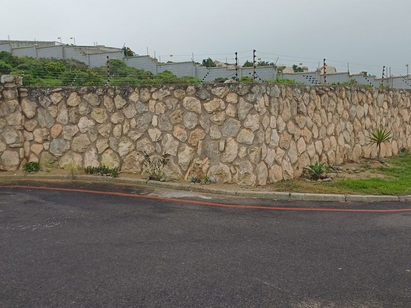 A view of the property boundary featuring a decorative stone wall topped with electric security fencing, adjacent to an asphalt road.