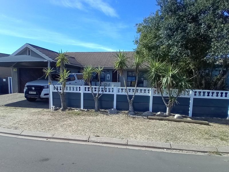 Front elevation of a single-story house featuring a tiled roof, a covered carport, and a modern boundary wall with a paved driveway.
