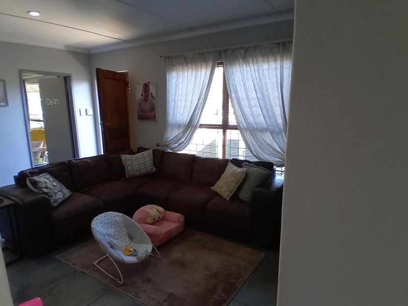 A living room area featuring tiled flooring, recessed lighting, and natural light through a window with curtain tracks.