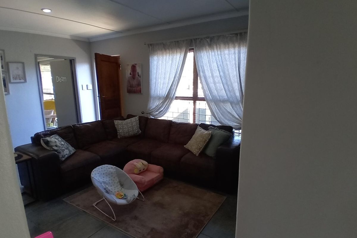 A living room area featuring tiled flooring, recessed lighting, and natural light through a window with curtain tracks.