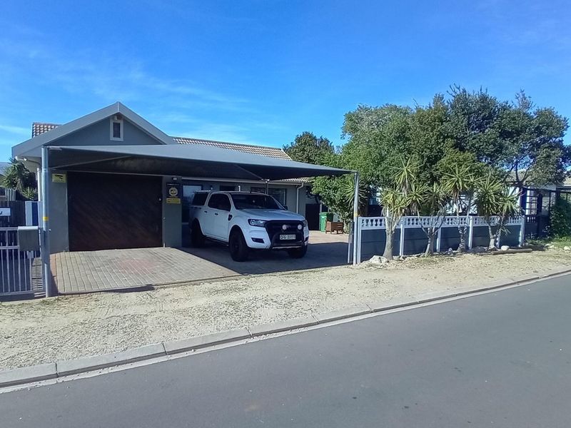 Front exterior view of the house featuring a paved driveway, a covered carport, and a secure boundary wall.