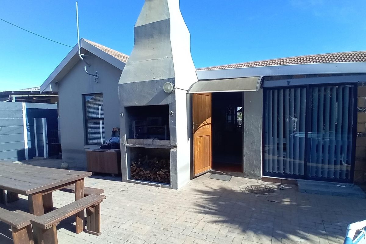 Rear exterior view featuring a paved patio area with a built-in braai, sliding door access, and tiled roof structure.