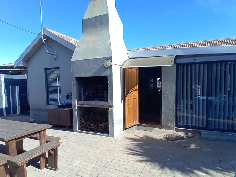 Rear exterior view featuring a paved patio area with a built-in braai, sliding door access, and tiled roof structure.