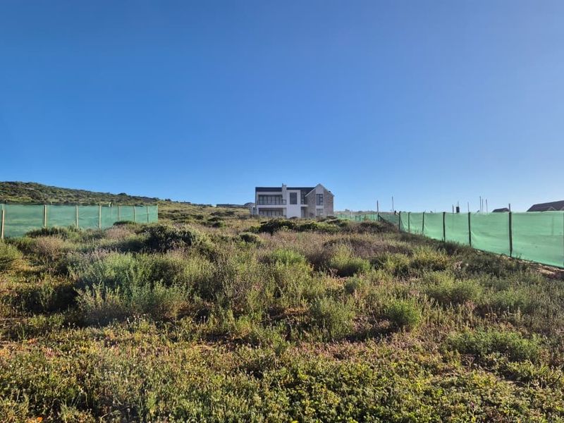 A view of a vacant residential plot featuring natural vegetation and perimeter fencing, with neighboring properties visible in the distance.