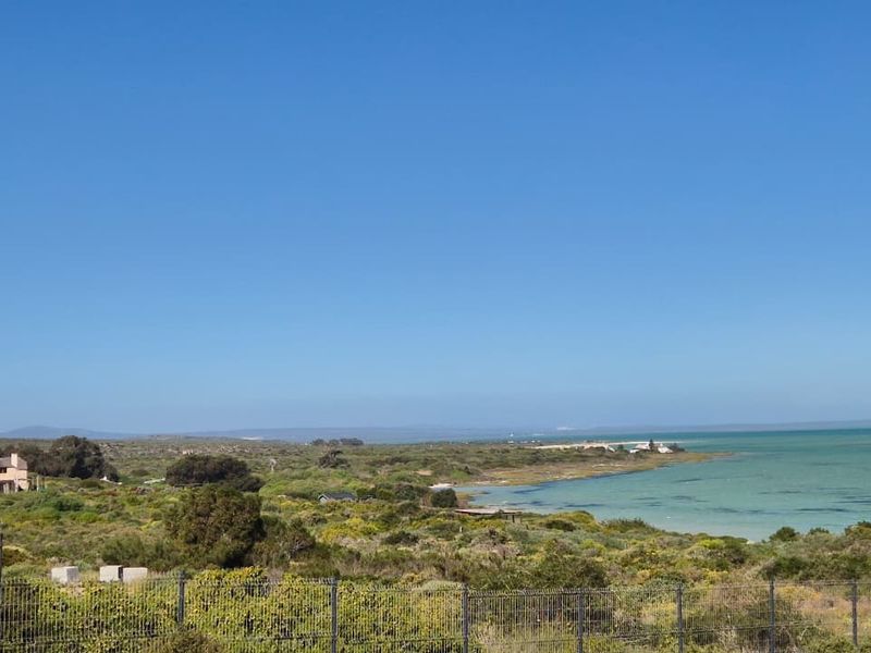 A scenic elevated view of the coastal landscape, featuring natural vegetation, a nearby lagoon, and distant shoreline.