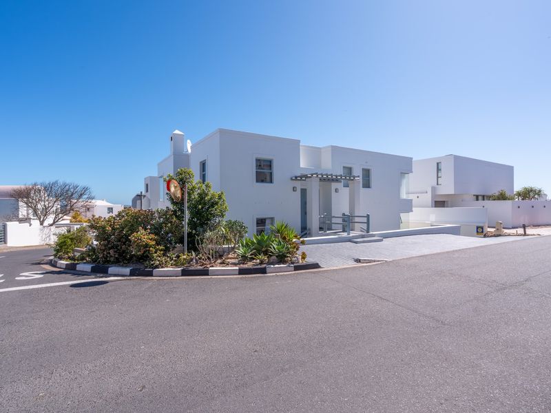 Modern white exterior facade featuring a paved driveway, pergola entrance, and clean architectural lines in a quiet residential street setting.
