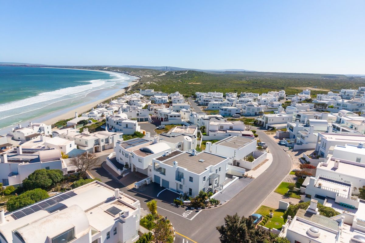 An aerial view of a coastal residential estate featuring white flat-roofed homes situated near the beach and ocean.