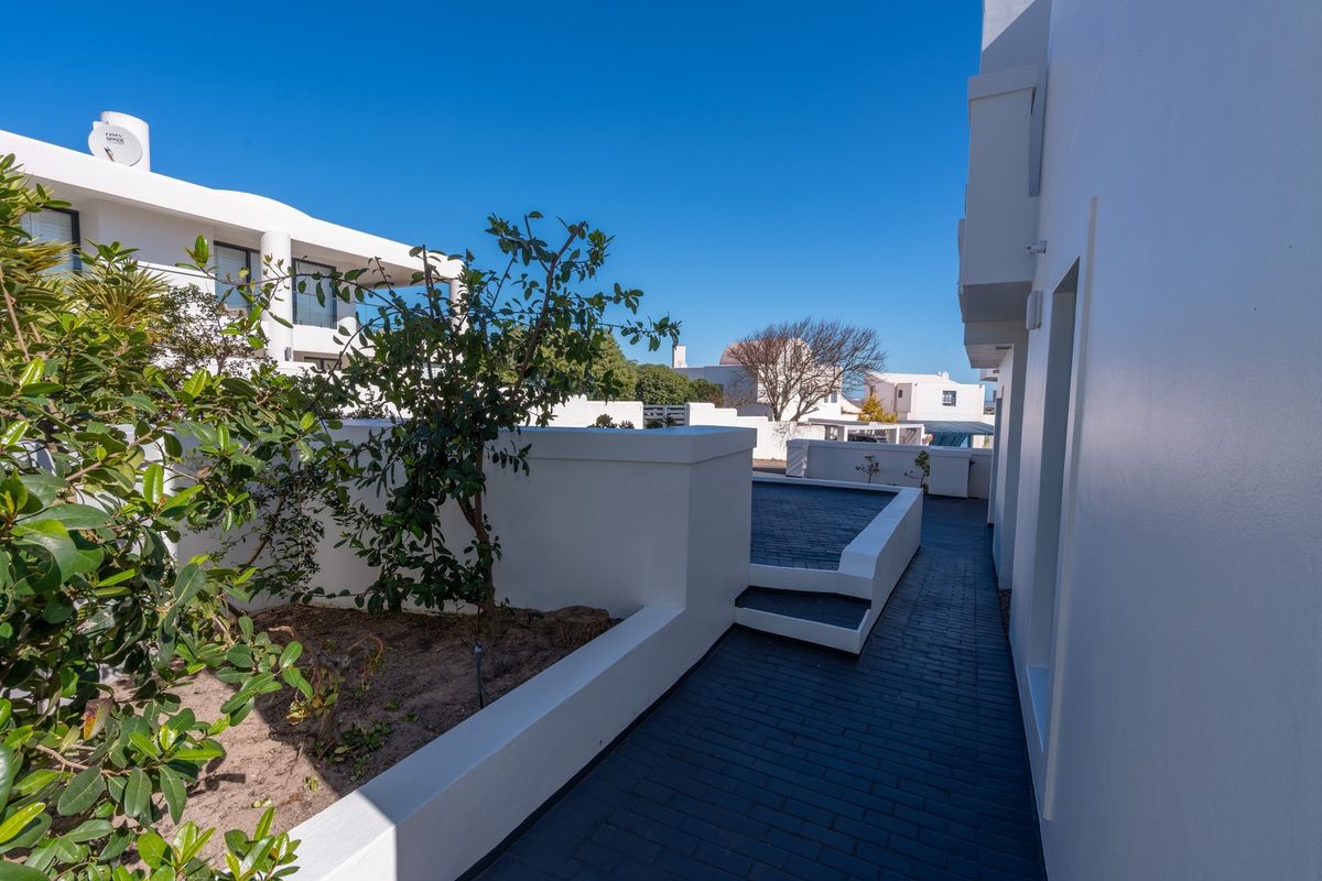 A clean, modern exterior rear area featuring a dark paved walkway, white rendered retaining walls, and a raised garden bed.