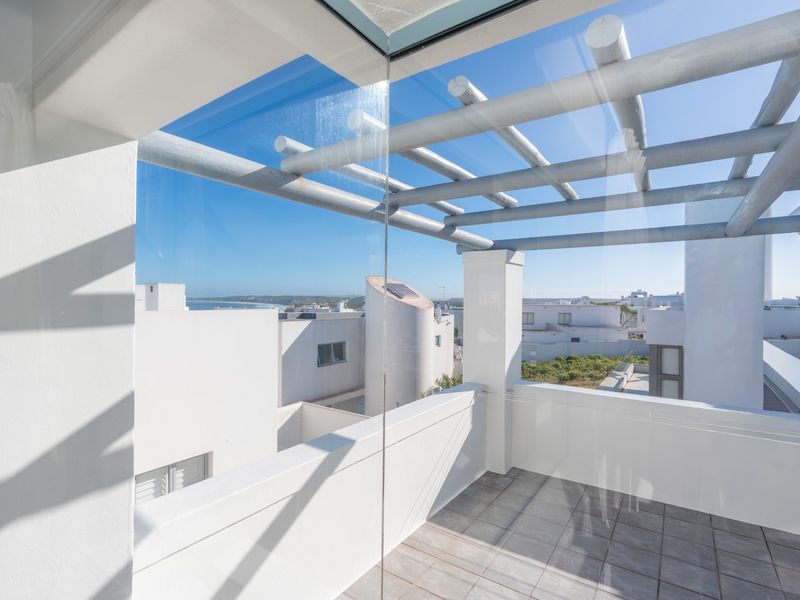 A modern, well-maintained balcony featuring a pergola structure, tiled flooring, and clear glass balustrades with views of the surrounding area.