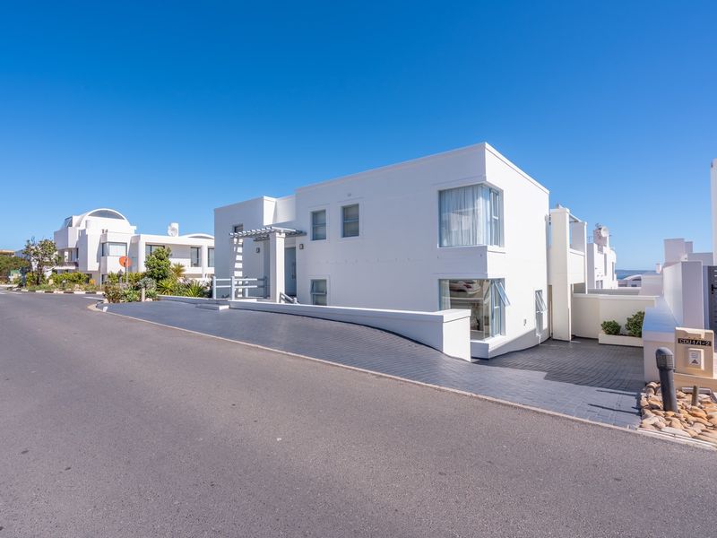 Modern white architectural facade featuring clean lines, corner windows, a paved driveway, and a pergola entrance in a well-maintained residential setting.