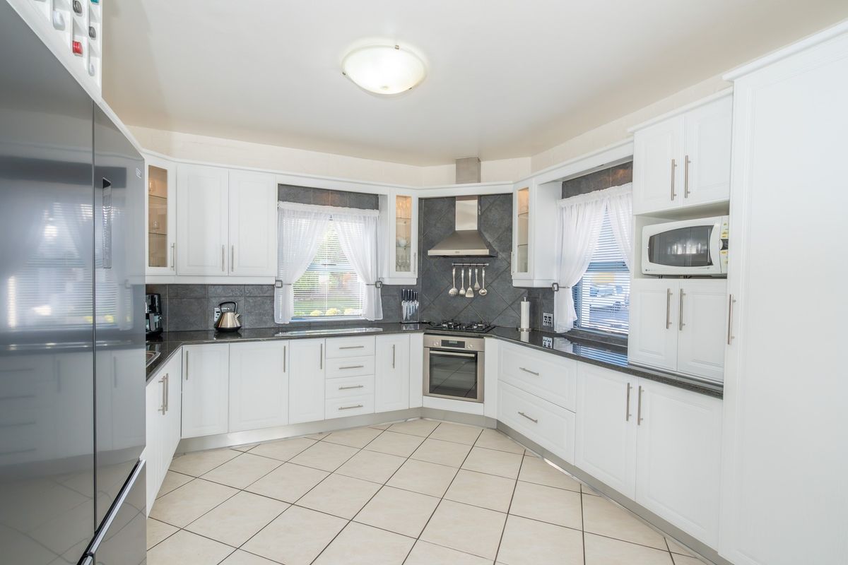 A well-maintained kitchen featuring white cabinetry, dark granite countertops, stainless steel appliances, and tiled flooring with a functional layout.