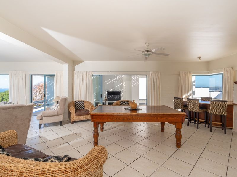 Spacious open-plan living area featuring tiled floors, a built-in bar, fireplace, and large sliding doors providing access to the outdoor area and ocean views.