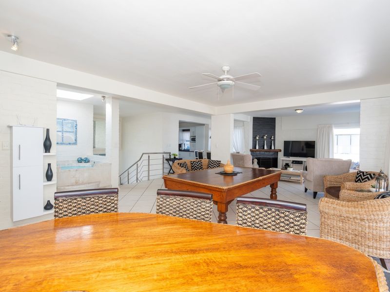 Spacious open-plan living area featuring tiled floors, a central fireplace, ceiling fan, and integrated shelving, creating a versatile and connected home environment.