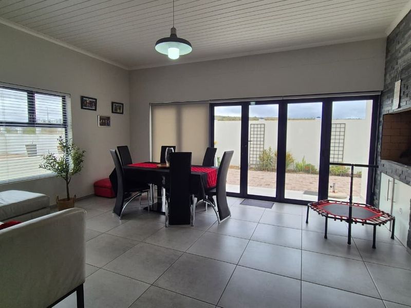 Spacious open-plan living and dining area featuring tiled floors, a stone-clad built-in braai, and large sliding doors providing seamless access to the outdoor patio.