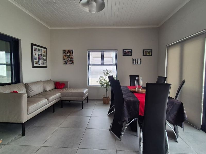 Spacious open-plan living and dining area featuring large sliding glass doors, neutral tiled flooring, and a classic tongue and groove ceiling.