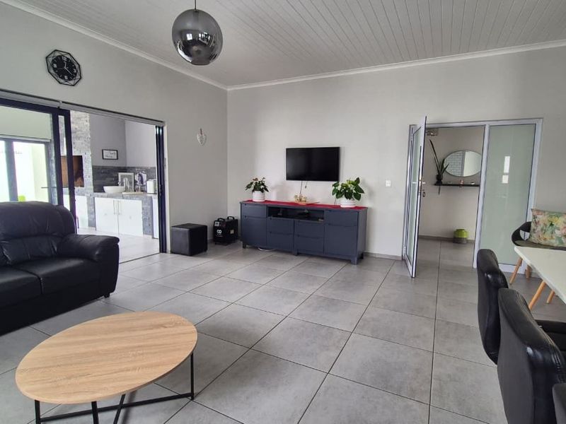 Spacious open-plan living area featuring large format floor tiles, a tongue and groove ceiling, and seamless access to adjacent rooms through sliding glass doors.