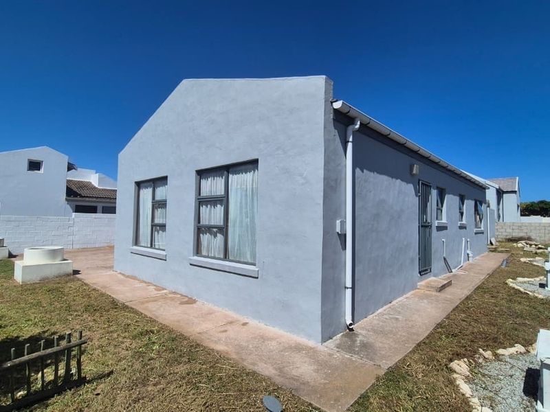 Rear view of the house showing the exterior facade, concrete pathways, and surrounding garden area with boundary walls.