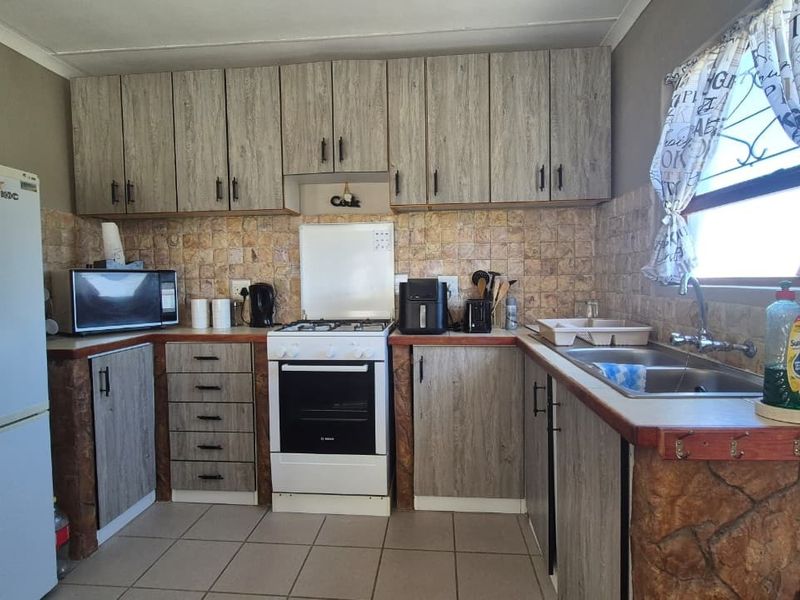 Functional kitchen featuring wood-look cabinetry, tiled backsplash, double basin sink, and a freestanding stove with tiled flooring.