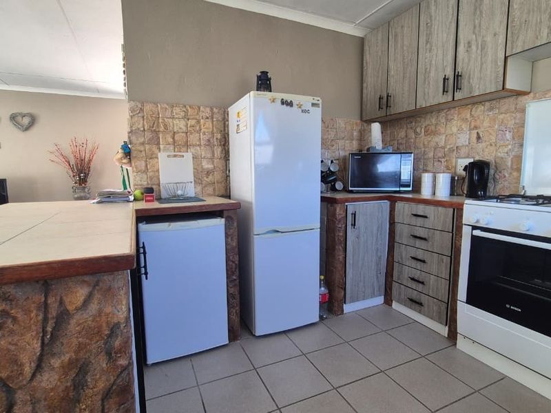 A functional kitchen featuring built-in cabinetry, a tiled backsplash, a gas stove with oven, and a breakfast counter with stone-look cladding.
