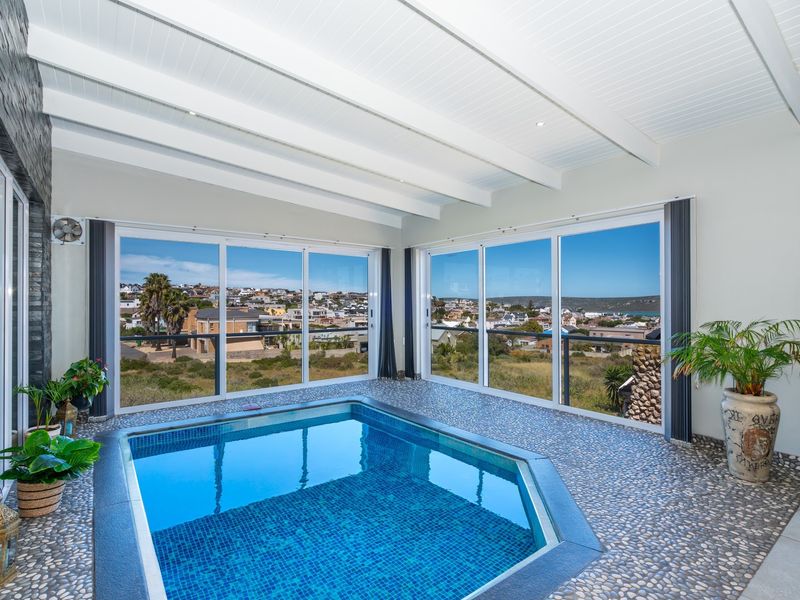 An indoor swimming pool area featuring mosaic tiling, pebble flooring, exposed beam ceilings, and large sliding glass doors offering panoramic coastal views.
