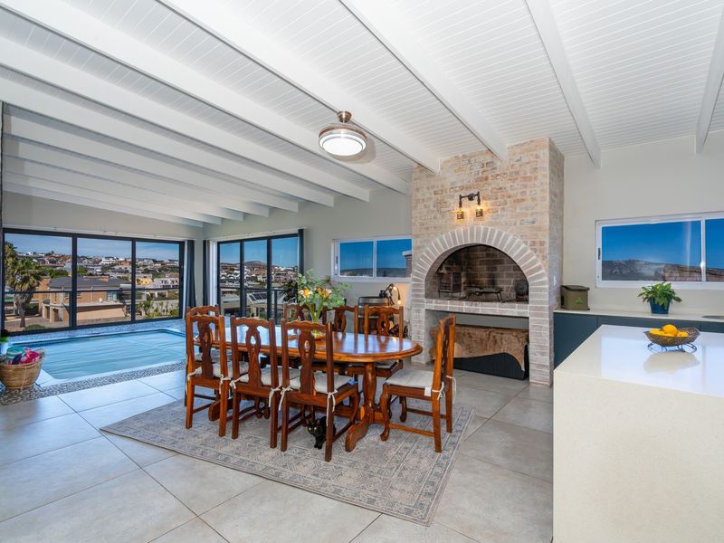 Spacious open-plan living and dining area featuring a brick fireplace, exposed beam ceiling, and large sliding doors opening to a pool deck.