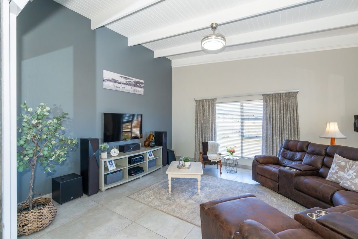 Spacious living room featuring high ceilings with exposed beams, a ceiling fan, and neutral tiled flooring, creating a bright and comfortable atmosphere.