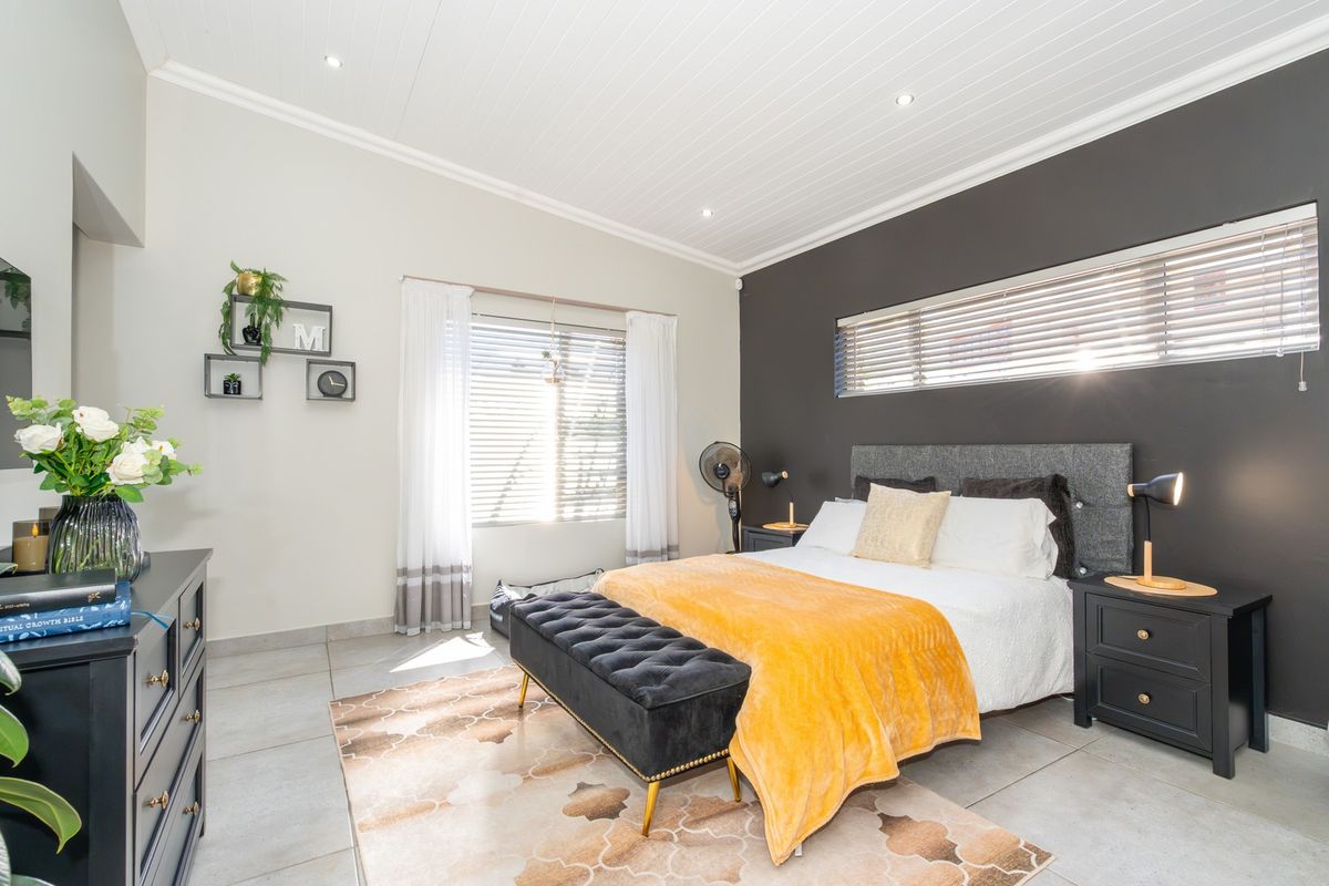 A well-maintained bedroom featuring tiled flooring, a tongue and groove ceiling with recessed lighting, and a dark accent wall with venetian blinds.