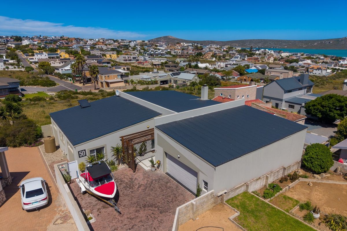 Aerial view of a modern residential property featuring a dark metal roof, solar panels, paved driveway, and a timber pergola entrance.