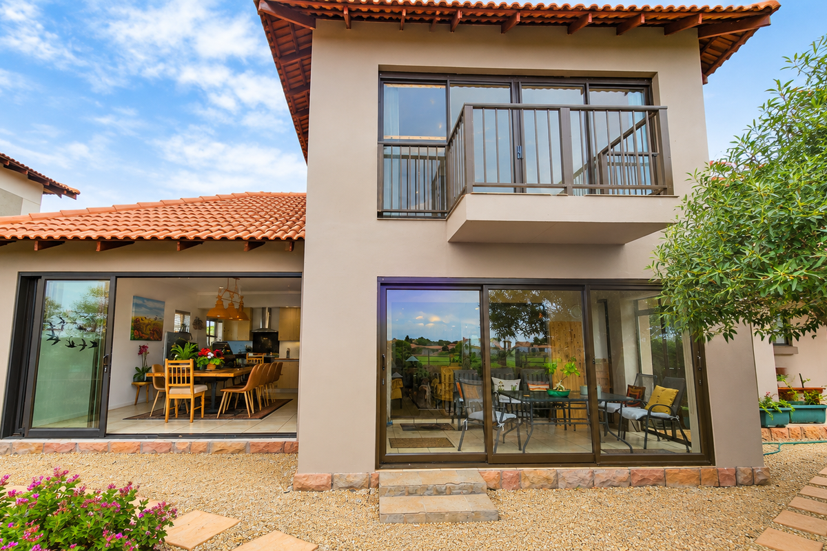 Rear view of a two-story house featuring terracotta roof tiles, a balcony with metal railings, and large sliding glass doors opening to the garden.