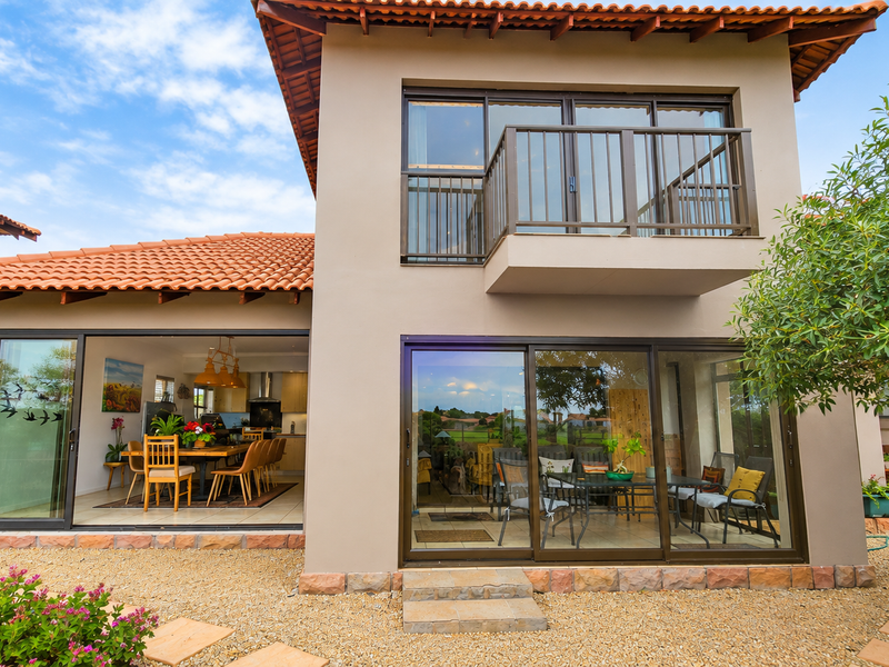 Rear view of a two-story house featuring terracotta roof tiles, a balcony with metal railings, and large sliding glass doors opening to the garden.