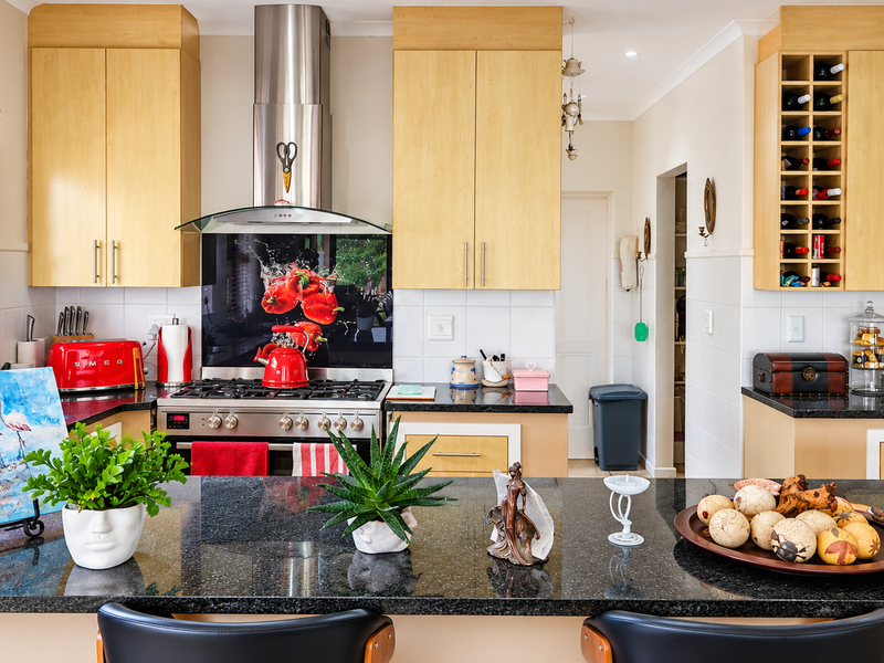 A well-maintained kitchen featuring light wood cabinetry, granite countertops, a stainless steel gas hob with extractor, and a dedicated built-in wine rack.
