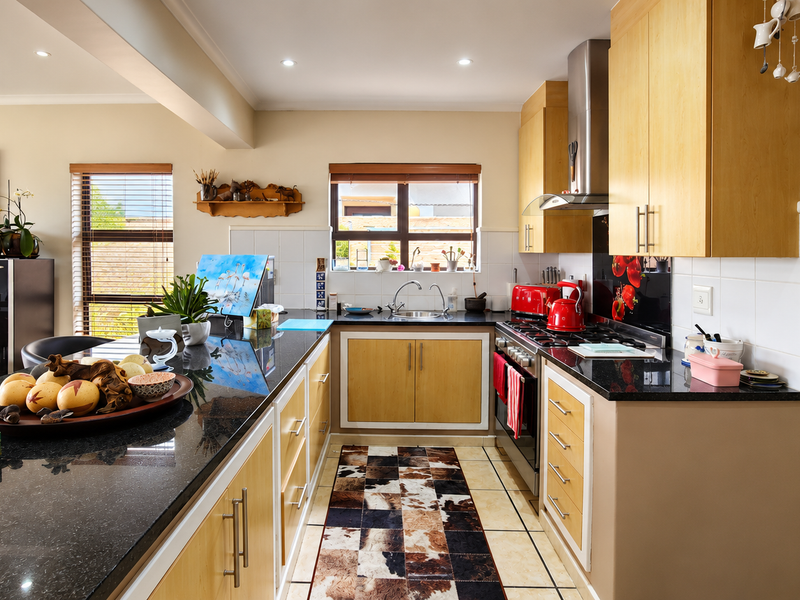 Spacious open-plan kitchen featuring granite countertops, light wood cabinetry, stainless steel appliances, and a functional layout with an adjacent scullery area.