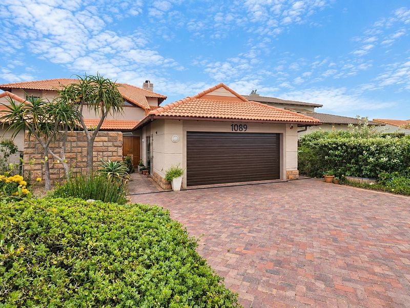 Front elevation of a well-maintained house featuring a paved driveway, automated garage, and attractive stone cladding accents with established garden landscaping.