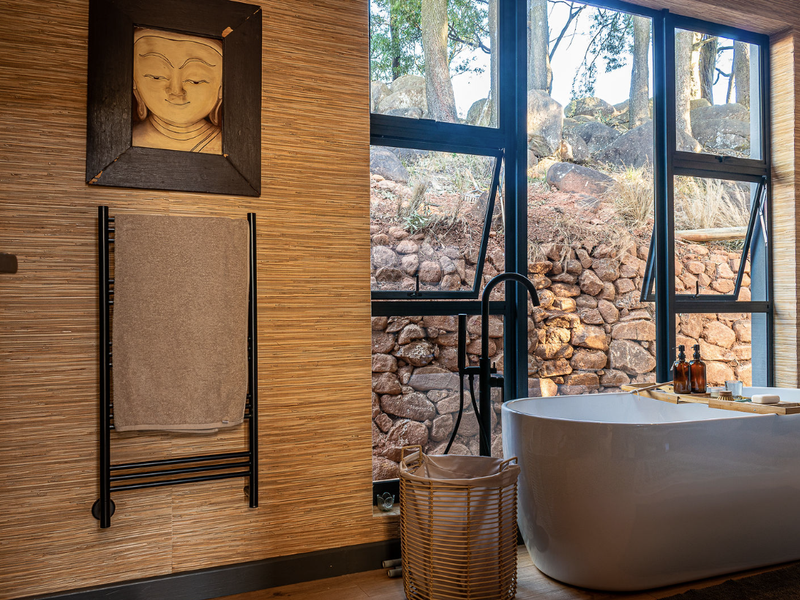 Modern bathroom featuring a sleek freestanding bathtub, black matte fixtures, and a heated towel rail, set against a natural stone garden backdrop.