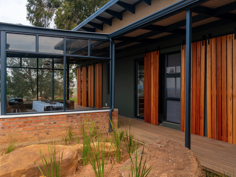 A modern covered patio featuring timber decking, exposed brickwork, and sliding timber shutters, providing a seamless transition between indoor and outdoor living spaces.