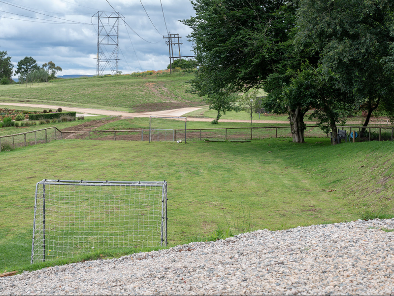 A spacious, well-maintained grassy garden area featuring mature trees and wooden post and rail perimeter fencing.