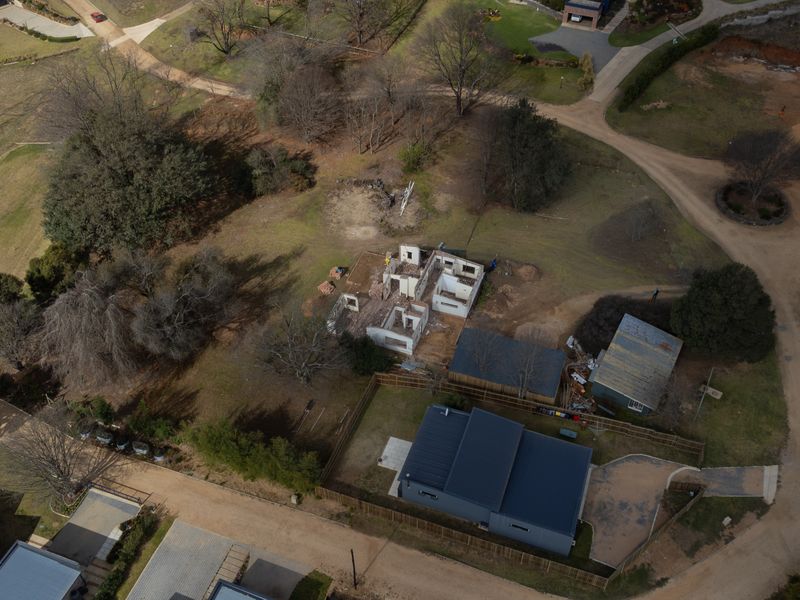 Aerial view of a residential property featuring an existing home and a partially constructed building shell on a spacious plot.