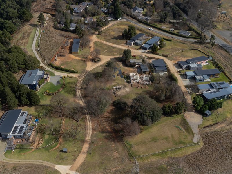 Aerial view of a residential estate featuring multiple dwellings, established landscaping, and unpaved access roads within a semi-rural setting.