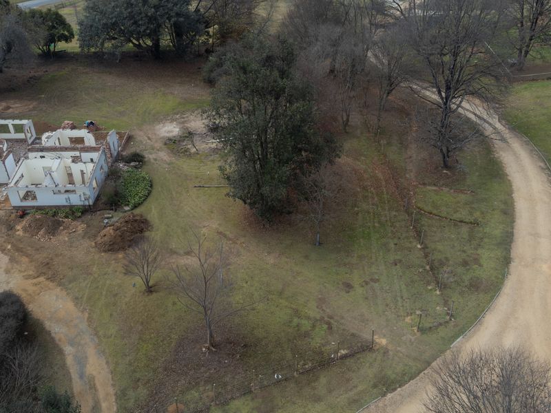 Aerial view of a vacant residential plot featuring a gravel driveway, mature trees, and the shell of a partially constructed building.