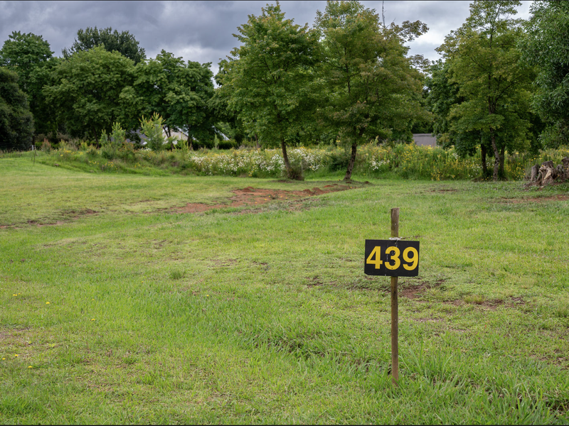A spacious, level residential vacant land plot featuring established trees and a well-maintained grass lawn, ideal for future development.