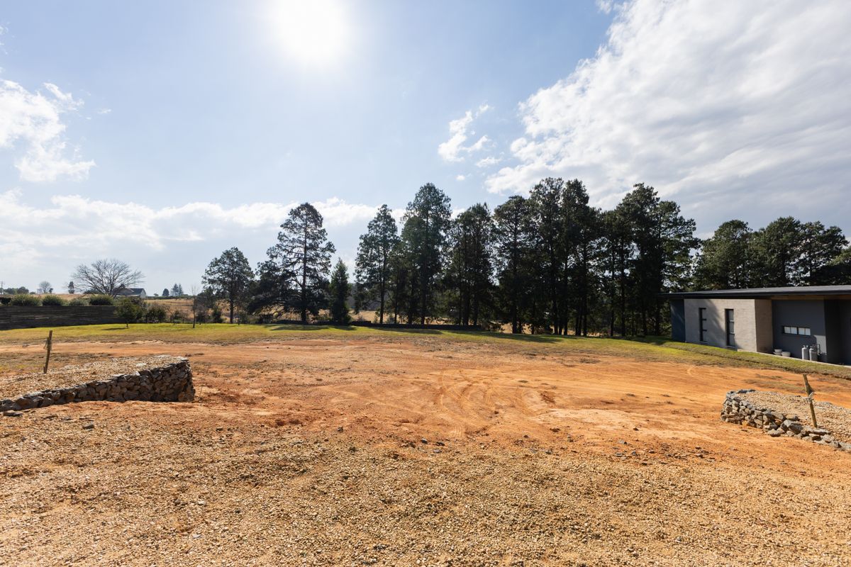 A spacious, cleared residential plot featuring gabion retaining walls and mature tree lines, offering a blank canvas for future development.