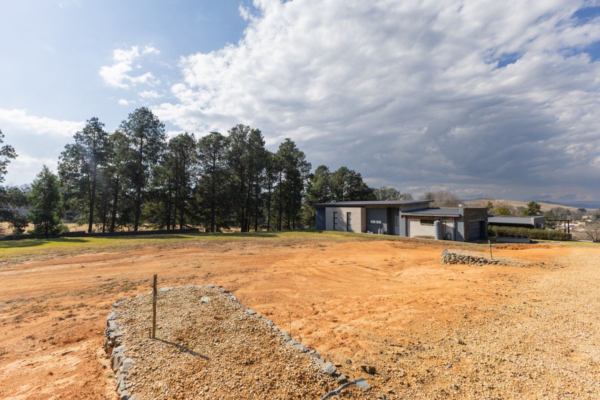 A wide-angle view of a residential property lot featuring a modern home, gravel landscaping, and a retaining wall structure.